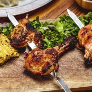 side view chicken kebab with greens lettuce tomato red onion grilled corn and dried barberry on the table